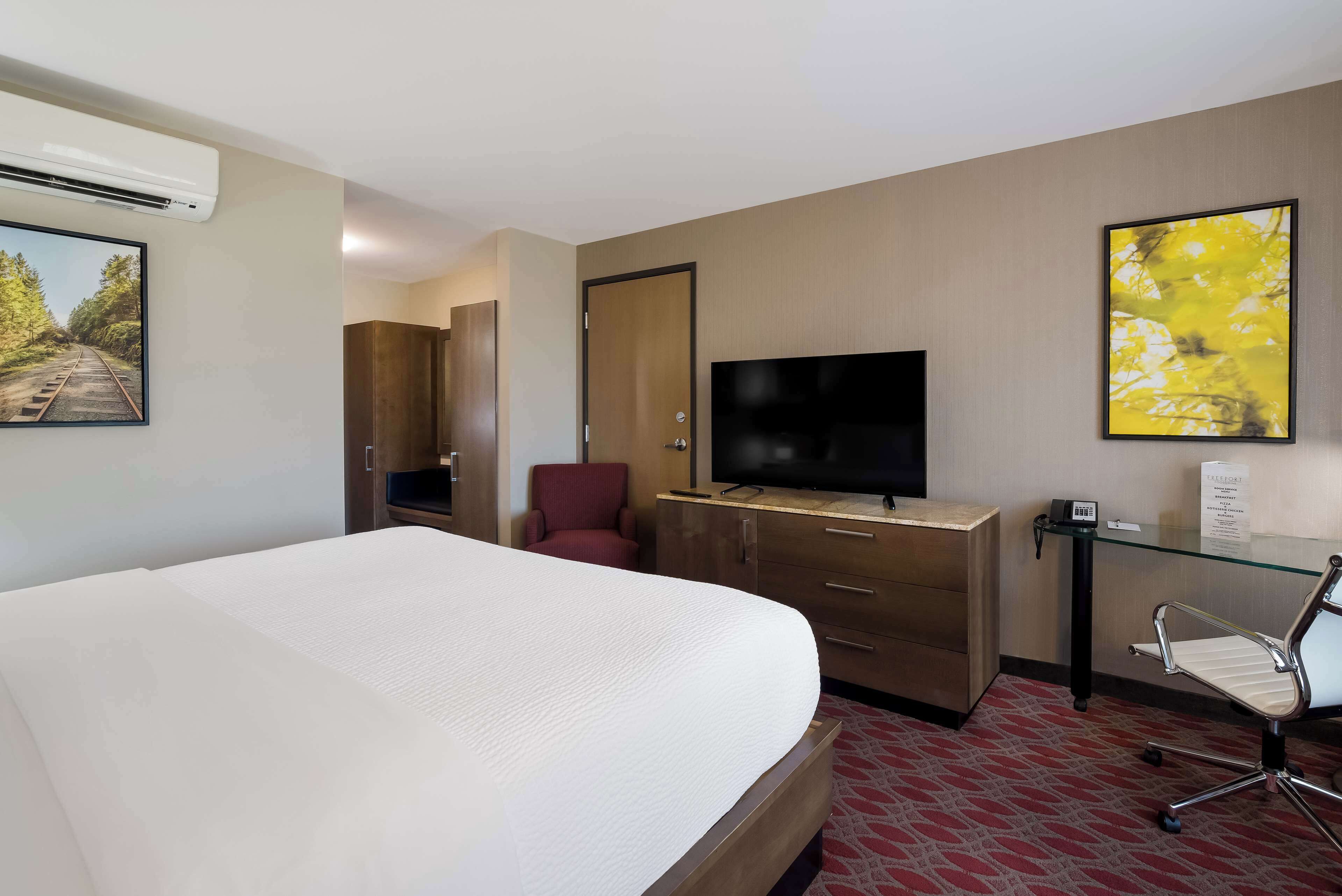 Een hotelkamer met een groot bed, een televisie, een bureau met stoel en een schilderij aan de muur.