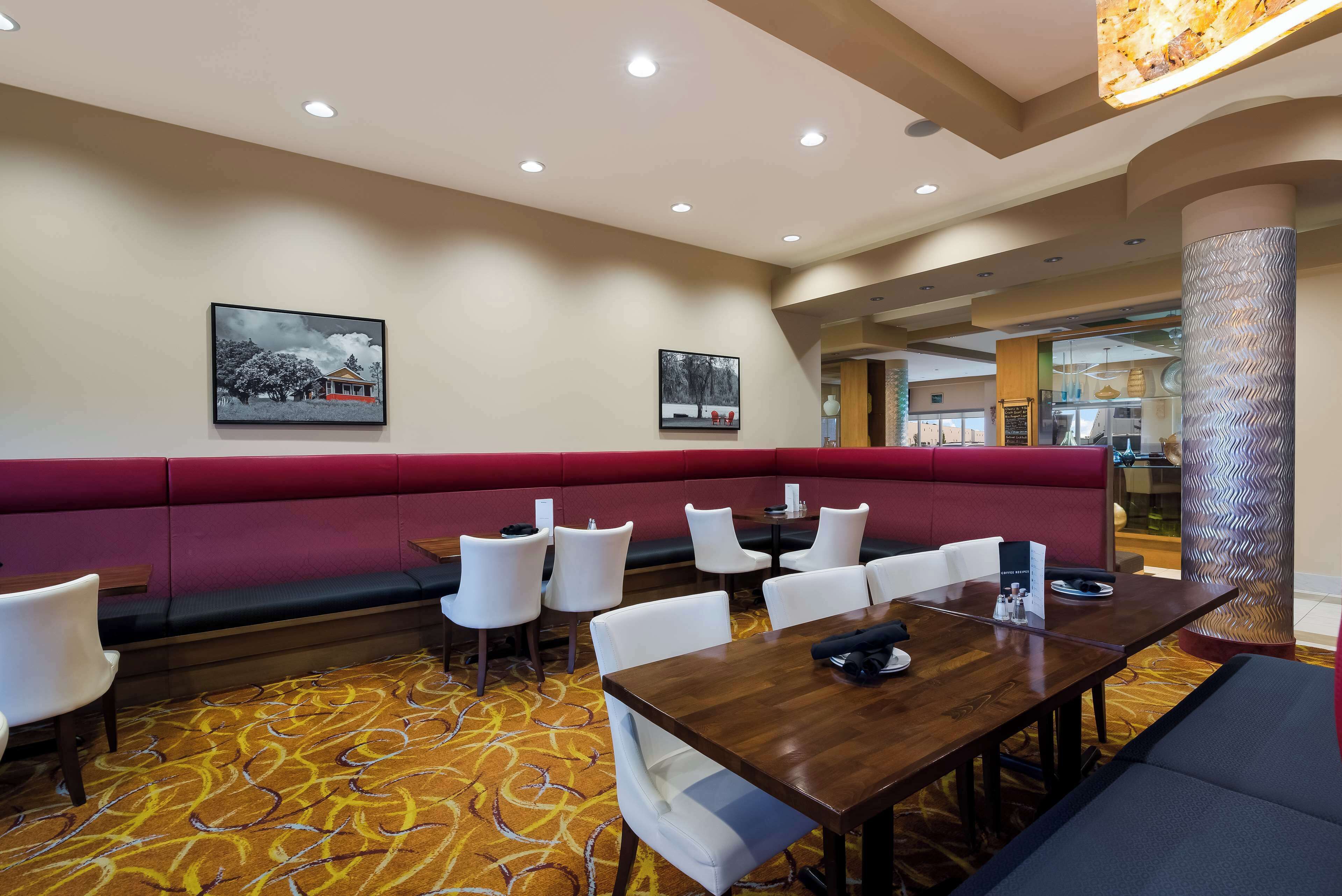 A hotel lobby with a red booth seating area, white chairs, and a wooden table.