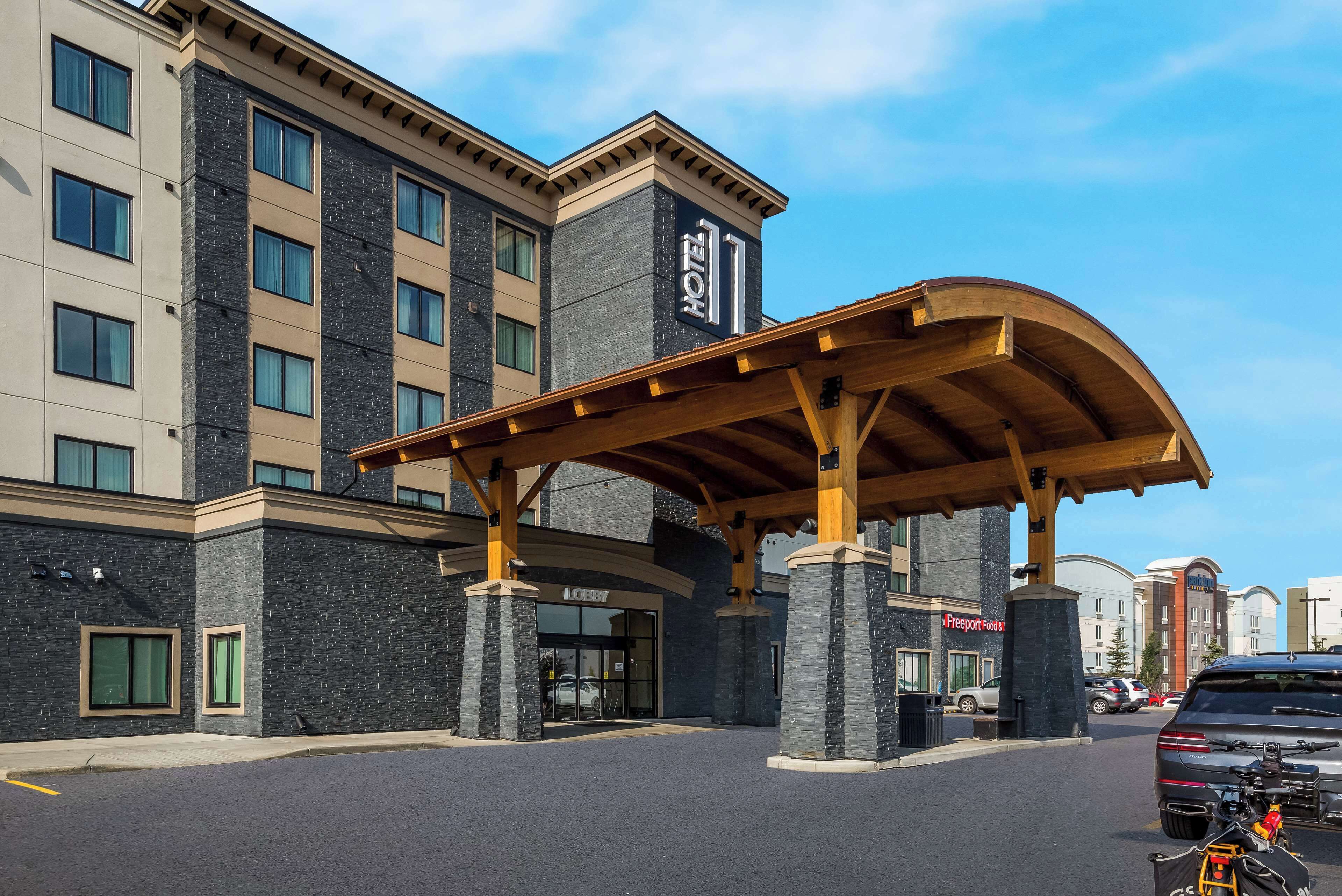 A hotel entrance with a covered waiting area, a stone facade, and a clear sky.