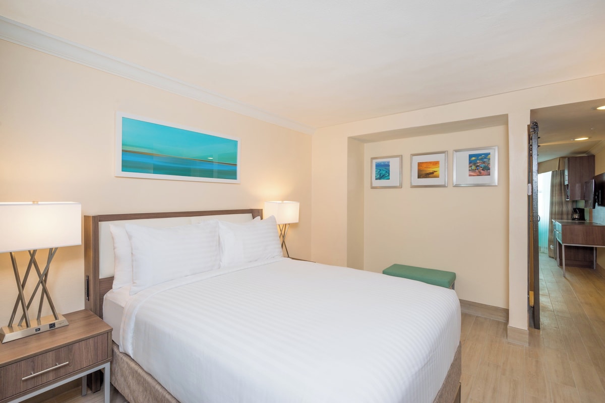 Ein Hotelzimmer mit einem Bett, Nachttischlampen, einer grünen Bank und Wandbildern.