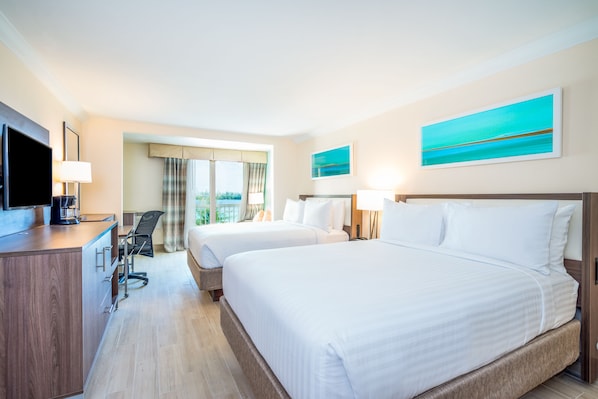Ein Hotelzimmer mit zwei Betten, einem Schreibtisch mit Fernseher und einem Sessel. An der Wand hängen zwei Gemälde.