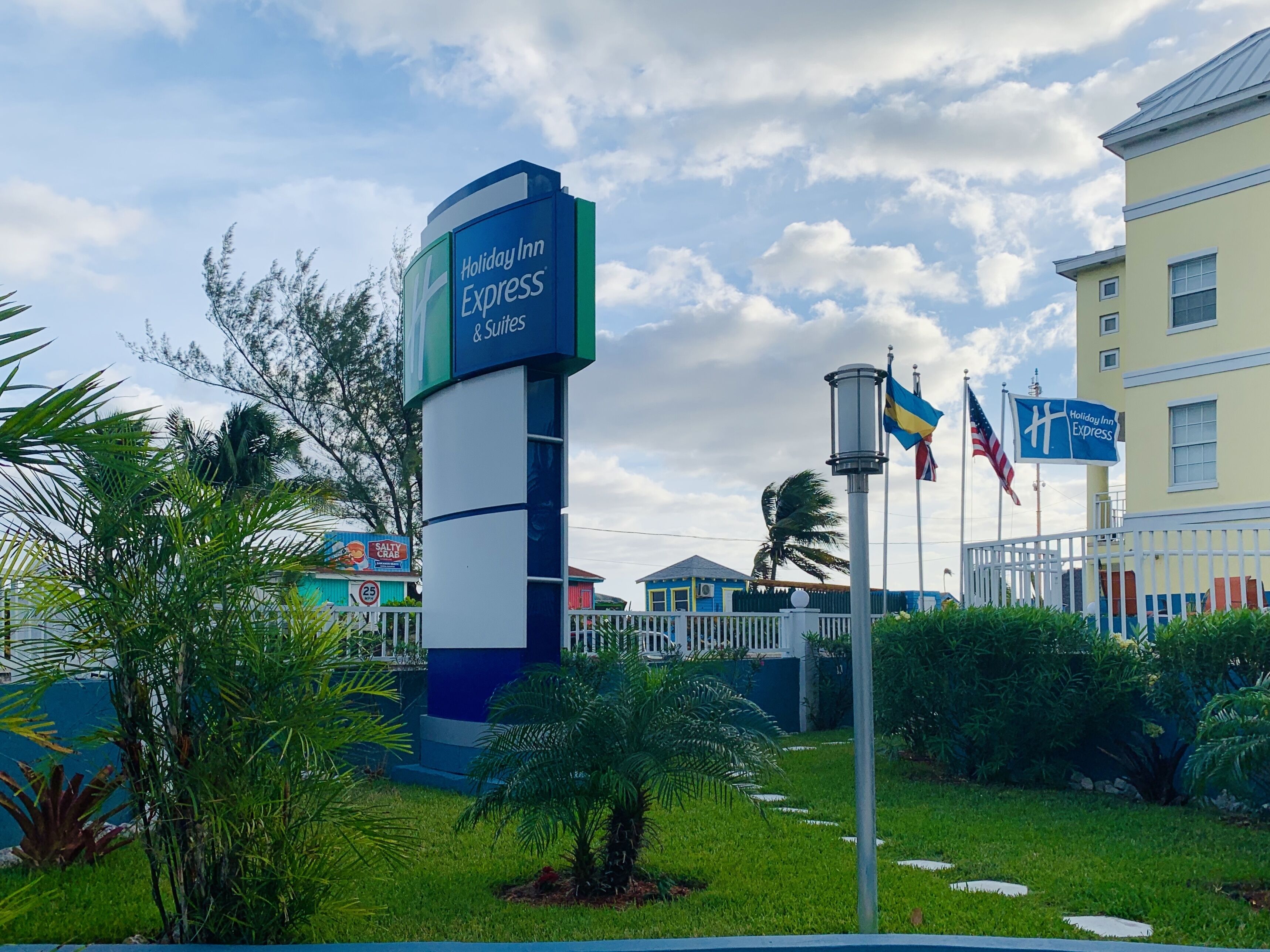 Señalización de Holiday Inn Express con un mástil de bandera, rodeada de follaje y un edificio al fondo.