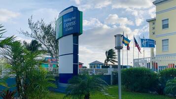 Señalización de Holiday Inn Express con un mástil de bandera, rodeada de follaje y un edificio al fondo.