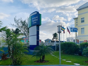 Ein Schild des Holiday Inn Express mit einer Flaggenpräsentation, umgeben von Grünpflanzen und einem Gebäude im Hintergrund.