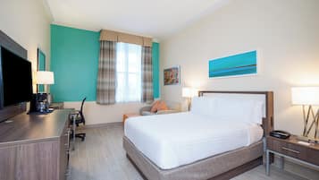 Une chambre d’hôtel avec un lit, un bureau doté d’une télévision, une chaise, une lampe et des œuvres d’art accrochées aux murs.