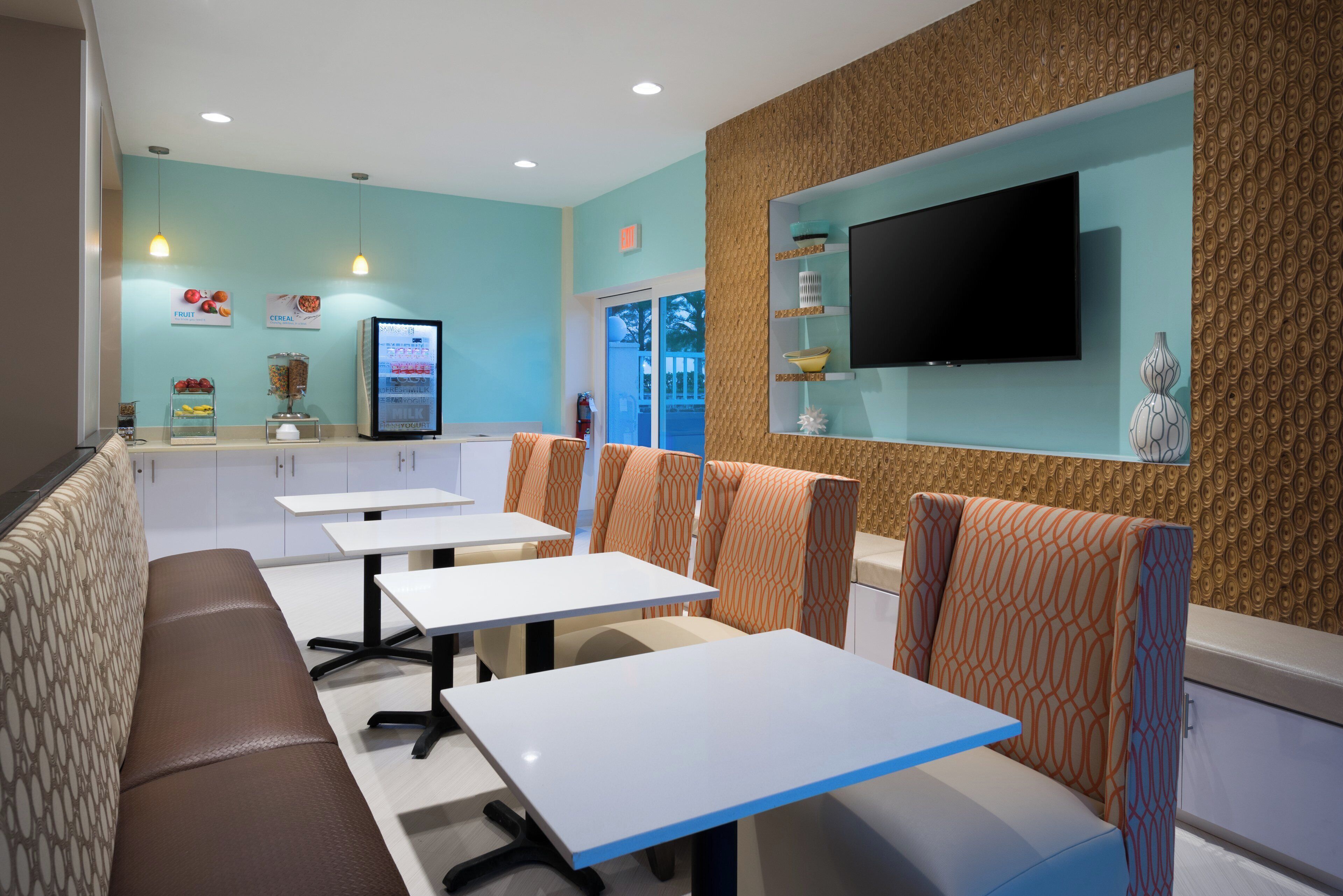 Un restaurant avec des banquettes et des tables, un téléviseur fixé au mur, et un présentoir de fruits et de céréales.
