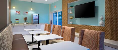 A restaurant with booths and tables, a wall-mounted TV, and a fruit and cereal display.