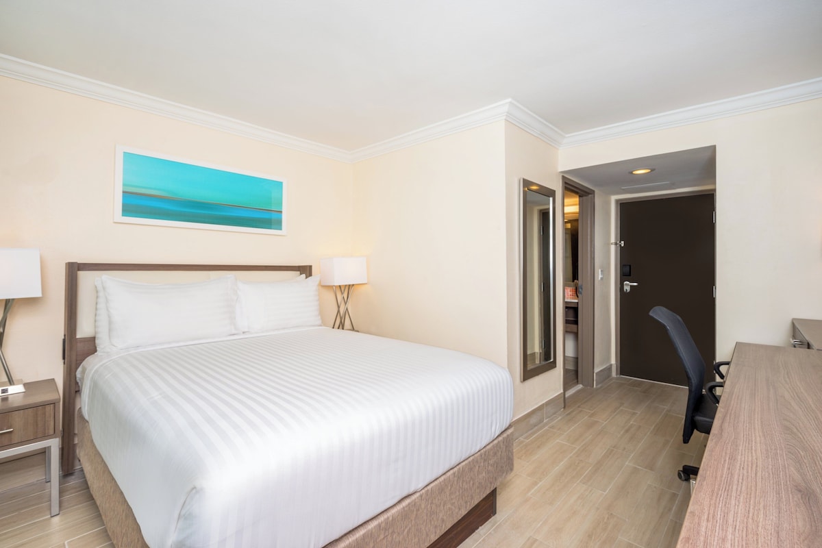 Ein Hotelzimmer mit einem großen Bett, Nachttischen, einem Schreibtisch und einer Tür zu einem Badezimmer.