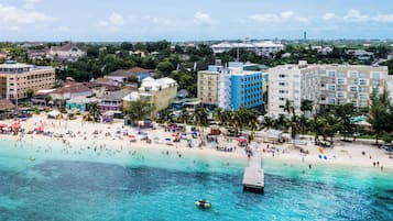 A beach with clear turquoise water, a pier, and buildings in the background.