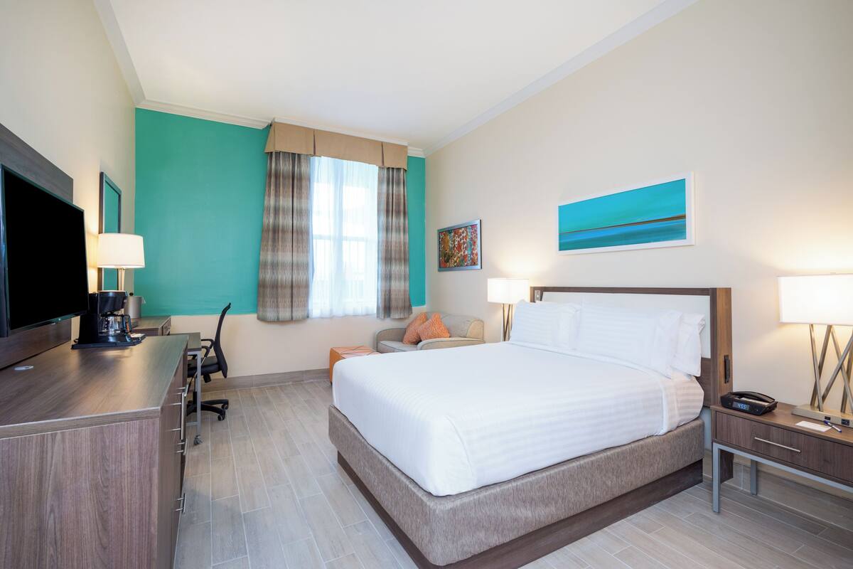 A hotel room with a large bed, a desk with a flat-screen TV, a coffee maker, and a chair.
