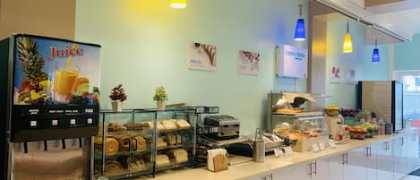 A breakfast bar with a juice dispenser, bread, eggs, and fruit display.
