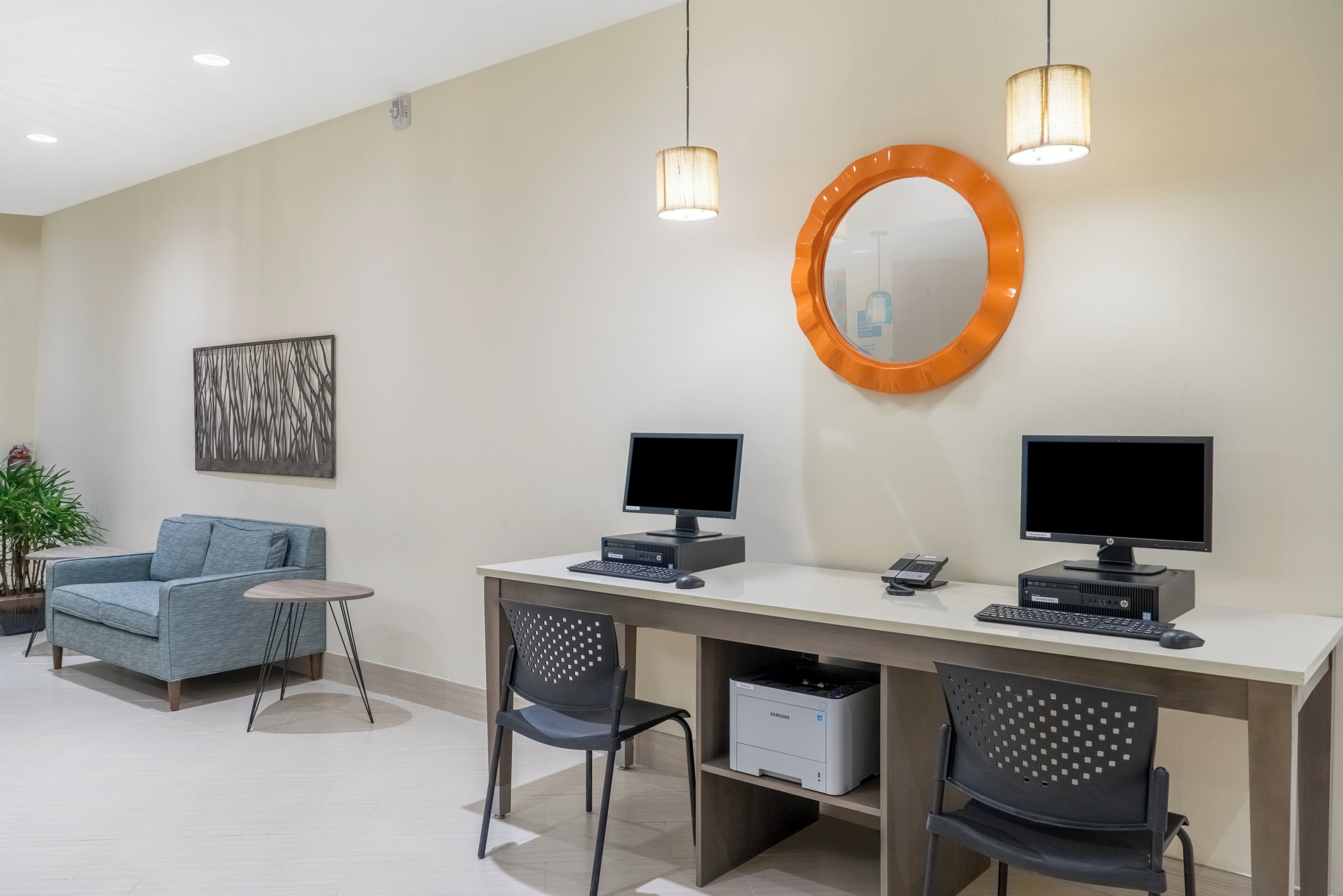 Un espace de bureau moderne comprenant deux bureaux, deux écrans d’ordinateur, un canapé bleu, une petite table ronde et un miroir décoratif.