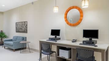 Un espace de bureau moderne comprenant deux bureaux, deux écrans d’ordinateur, un canapé bleu, une petite table ronde et un miroir décoratif.