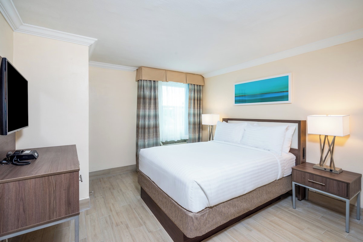Ein Hotelzimmer mit Bett, Nachttischen, Fernseher und einem Gemälde an der Wand.