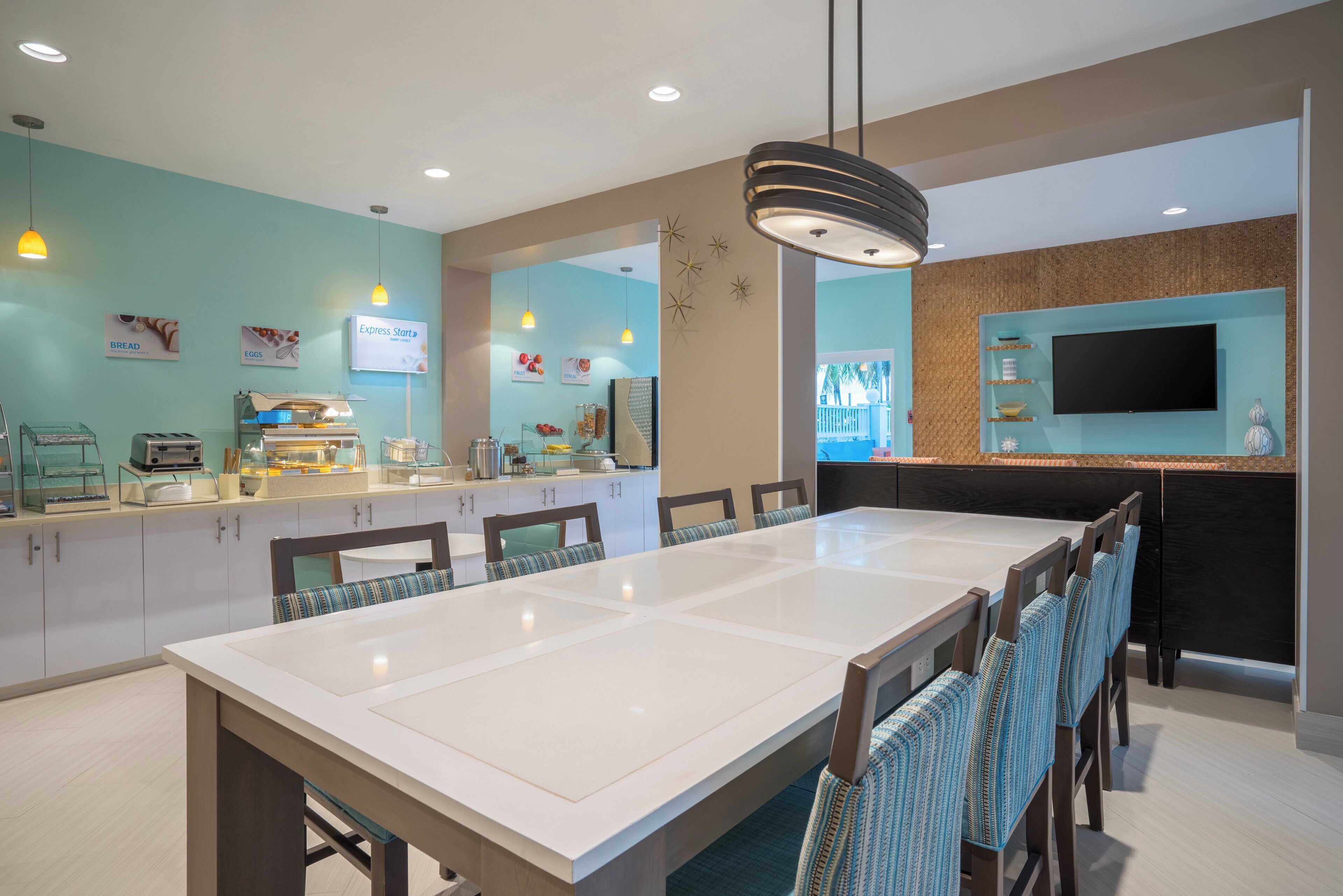 A modern dining area with a long table, chairs, a buffet counter, and a television mounted on the wall.