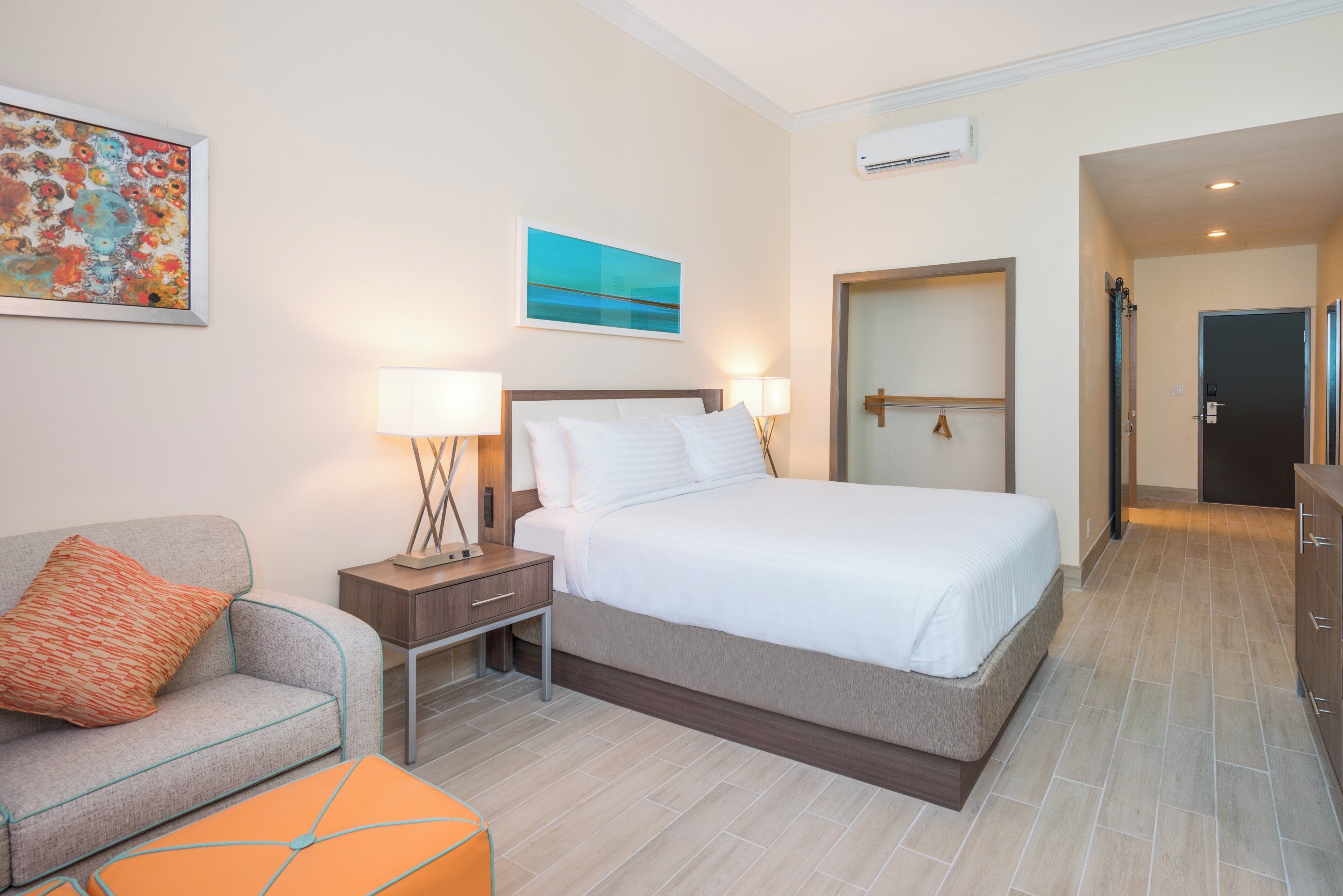 A hotel room with a bed, a nightstand with lamps, a sofa, and a painting on the wall.