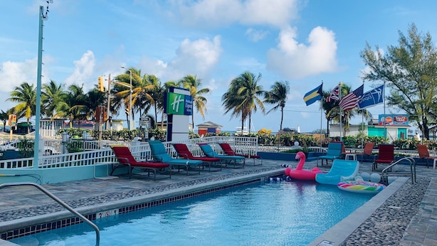 A swimming pool with lounge chairs, a flamingo float, and flags. - Holiday Inn Express & Suites Nassau by IHG (Nassau)