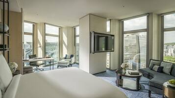 A modern hotel room with a large bed, a desk with a laptop, a sofa, and a TV mounted on the wall.