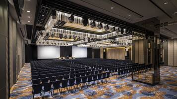 A conference room with rows of chairs, a stage, and a chandelier.