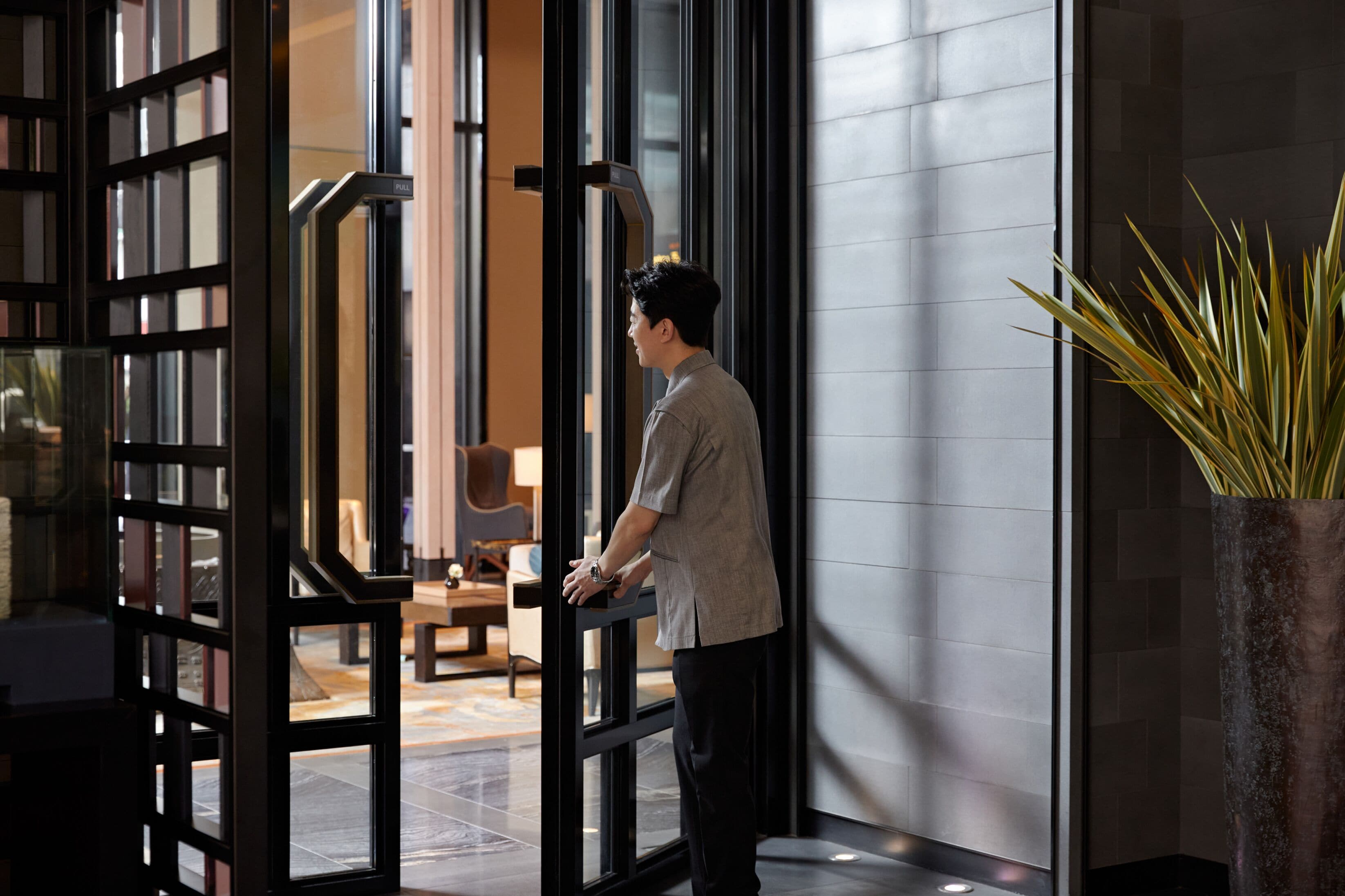 A man standing at a glass door with a modern interior visible through it.