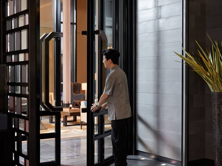 A man standing at a glass door with a modern interior visible through it.
