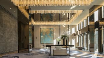 A spacious lobby with a high ceiling, a large abstract painting, a reception desk, and a modern chandelier.