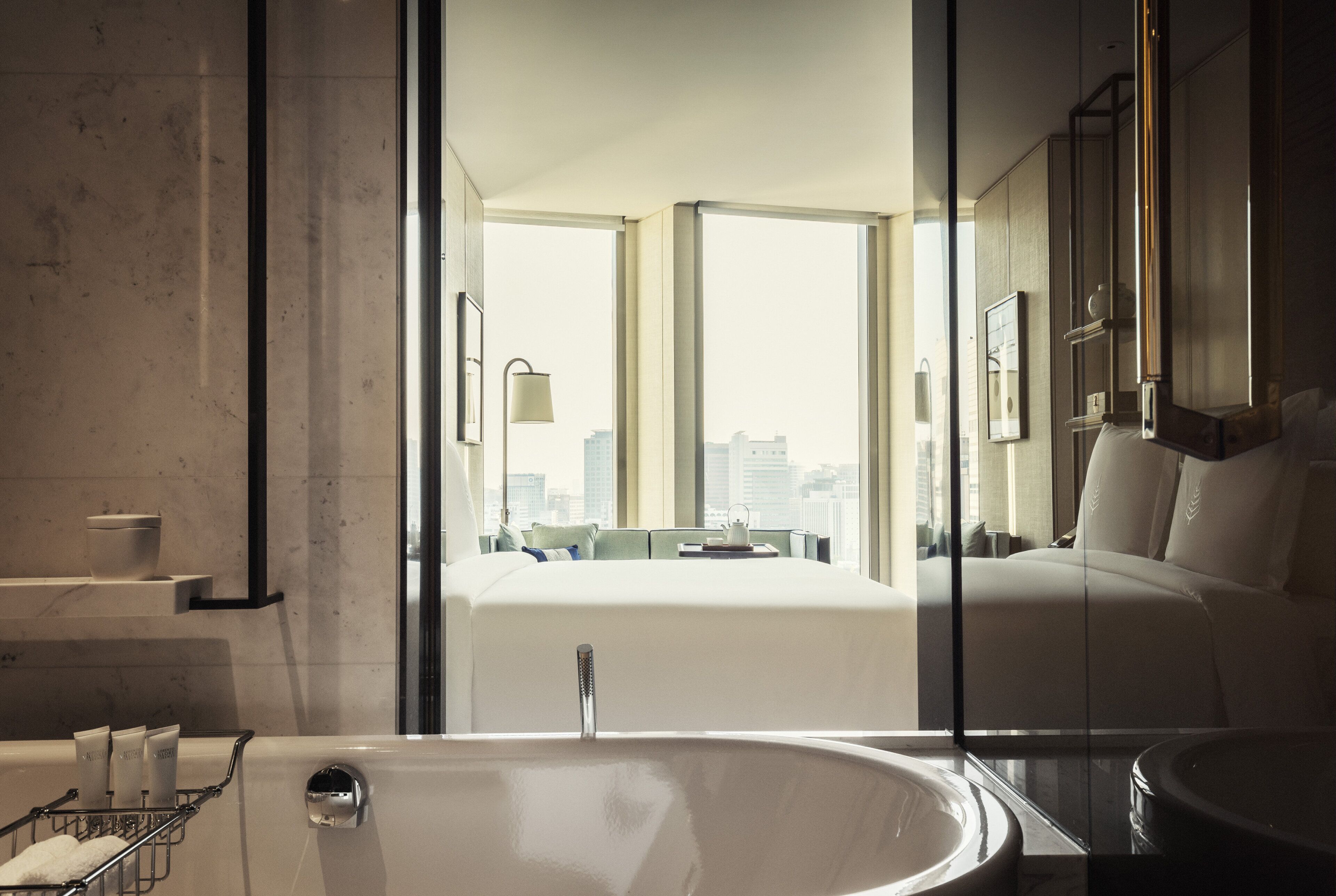 A modern bathroom with a large bathtub, a glass shower enclosure, and a city view.