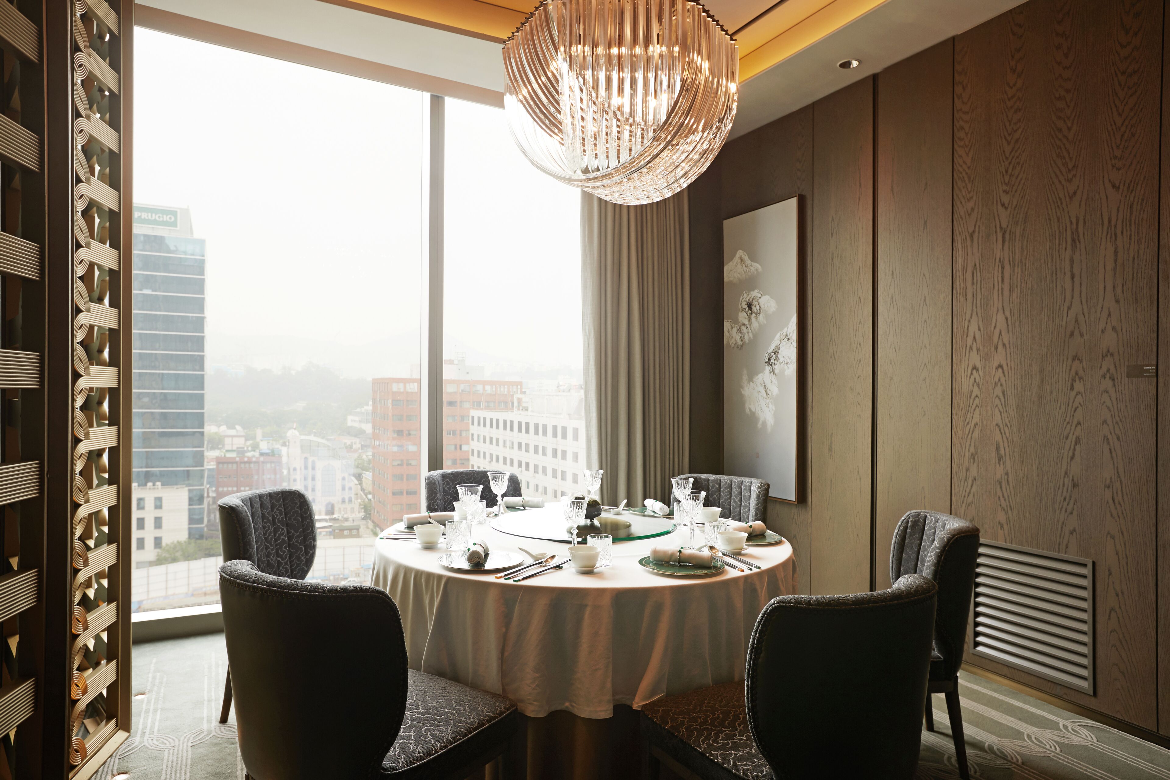 A dining area with a round table set for four, large windows, and a view of the cityscape.