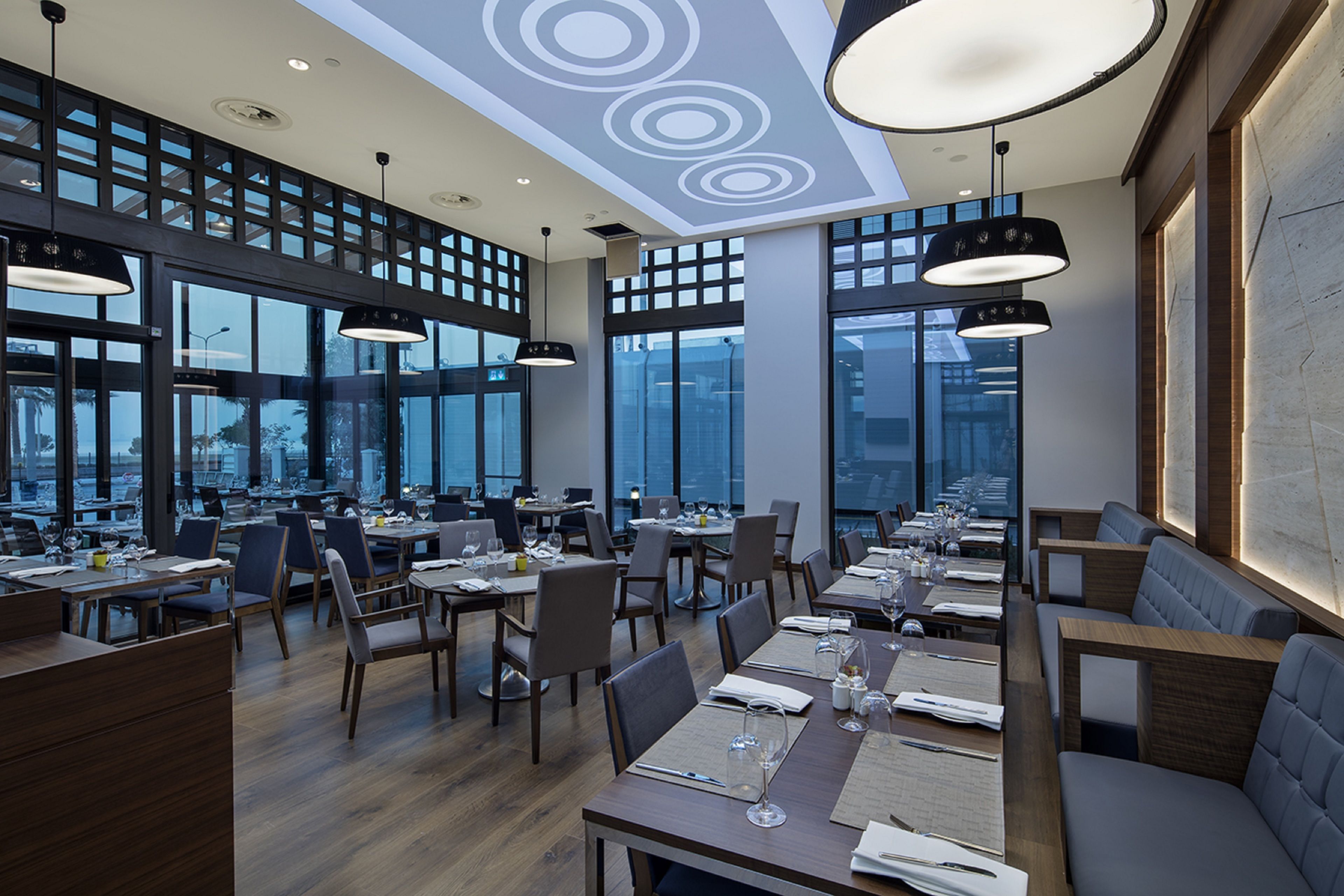 A modern restaurant with high ceilings, large windows, and a variety of seating options including tables and booths.