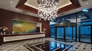 A modern lobby with a reception desk, a large abstract painting, a glass elevator, and a reflective floor. - Hilton Garden Inn Izmir Bayrakli (Izmir)