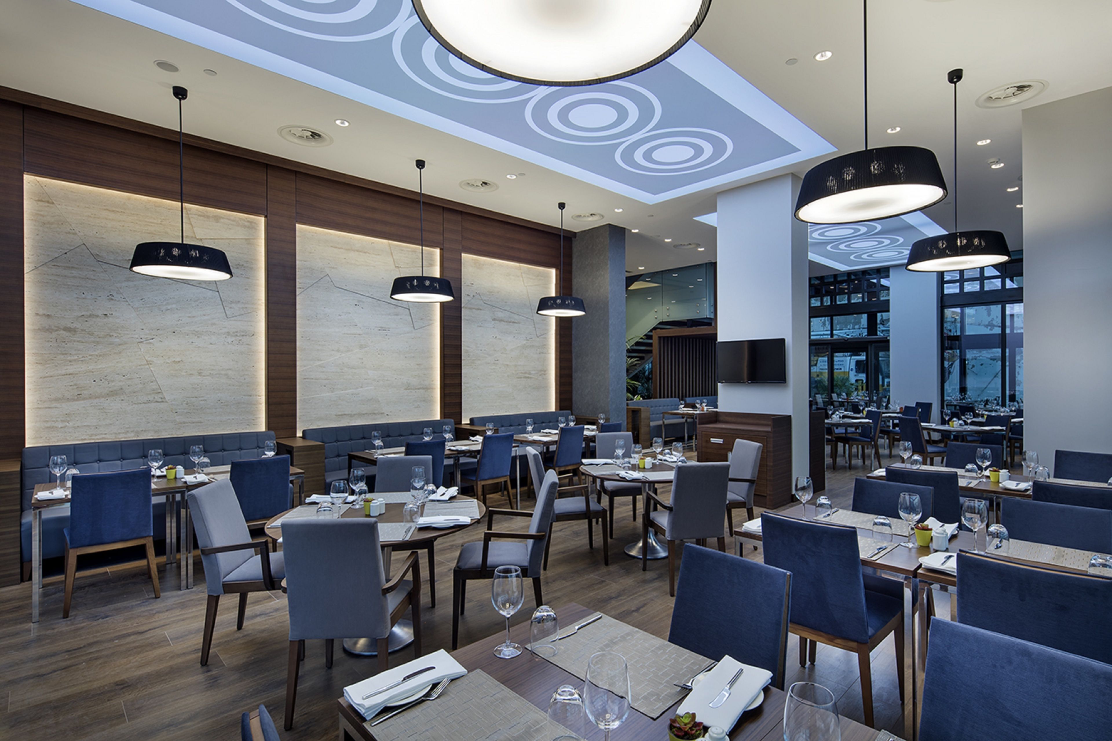A modern restaurant with multiple dining areas, wooden flooring, and contemporary pendant lighting.