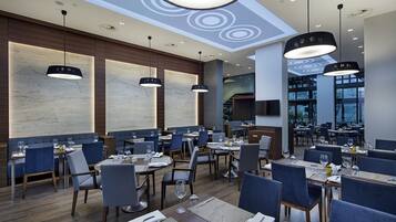 A modern restaurant with multiple dining areas, wooden flooring, and contemporary pendant lighting.