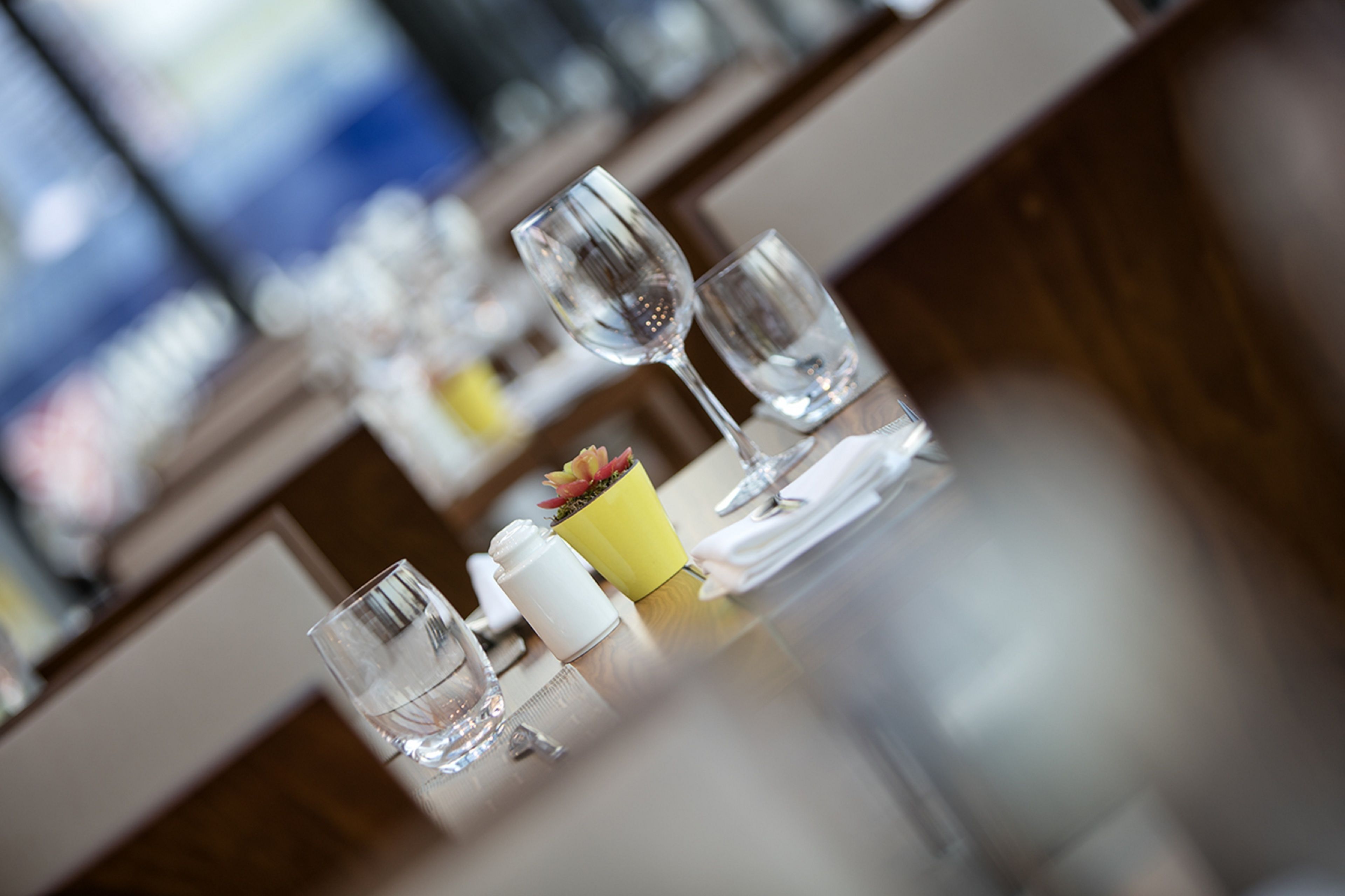 A dining table with a yellow flower vase, clear glasses, and a white bottle, likely containing water or a beverage.