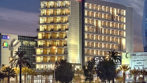 A modern hotel with multiple floors, a prominent vertical sign, and a waterfront view. - Hilton Garden Inn Izmir Bayrakli (Izmir)