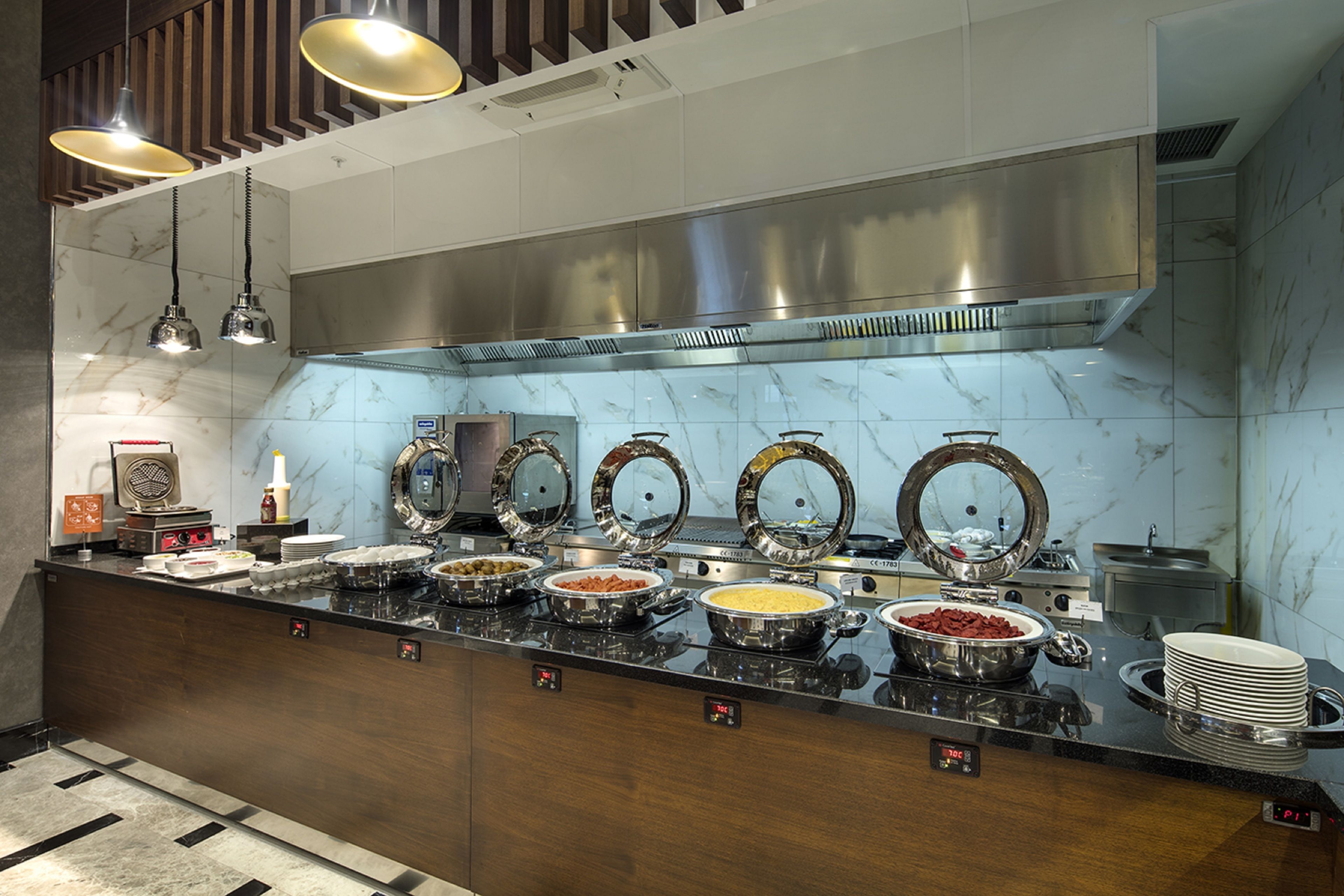 A buffet setup with multiple serving stations, a stainless steel range hood, and a marble backsplash.