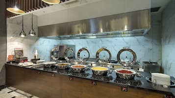 A buffet setup with multiple serving stations, a stainless steel range hood, and a marble backsplash.