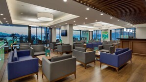 A modern hotel lobby with seating areas, a bar, and large windows offering a view of the cityscape. - Hilton Garden Inn Izmir Bayrakli (Izmir)