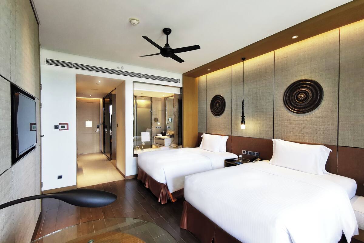 A hotel room with two beds, a ceiling fan, a large mirror, and a modern design.
