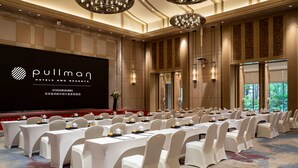 A conference room with rows of tables and chairs, a large screen displaying the hotel name, and a carpeted floor. - Pullman Resort Xishuangbanna (Xishuangbanna Dai)