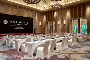 A conference room with rows of tables and chairs, a large screen displaying the hotel name, and a carpeted floor. - Pullman Resort Xishuangbanna (Xishuangbanna Dai)
