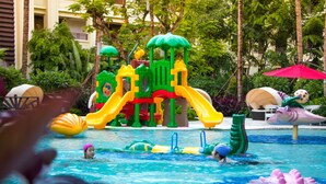 Een zwembadgedeelte met een speelstructuur in het water, inclusief glijbanen en een zwemband in de vorm van een zeemonster.