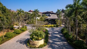 A pathway leading to a traditional-style building surrounded by lush greenery and palm trees. - Pullman Resort Xishuangbanna (Xishuangbanna Dai)