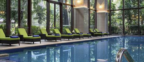 An indoor swimming pool with lounge chairs and large windows.
