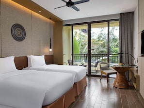 A hotel room with two beds, a balcony with a table and chairs, and a view of greenery outside.