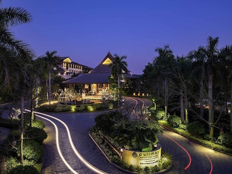 Un hôtel doté d’une allée d’accès sinueuse, de palmiers et d’une enseigne indiquant « Pullman Hotel & Resort ».. Pullman Resort Xishuangbanna