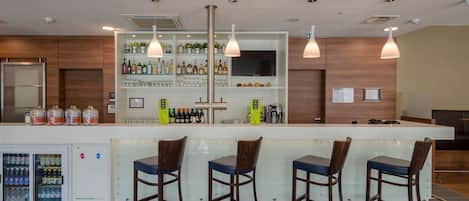 Zona de bar moderna con barra, taburetes y dispensador de bebidas.