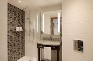 Une salle de bain moderne dotée d’une douche à parois de verre, d’un lavabo en granit et d’un grand miroir.