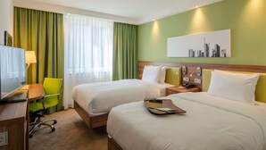 A hotel room with two beds, a desk with a chair, a television, and a cityscape painting on the wall. - Hampton by Hilton Frankfurt City Centre (Frankfurt)