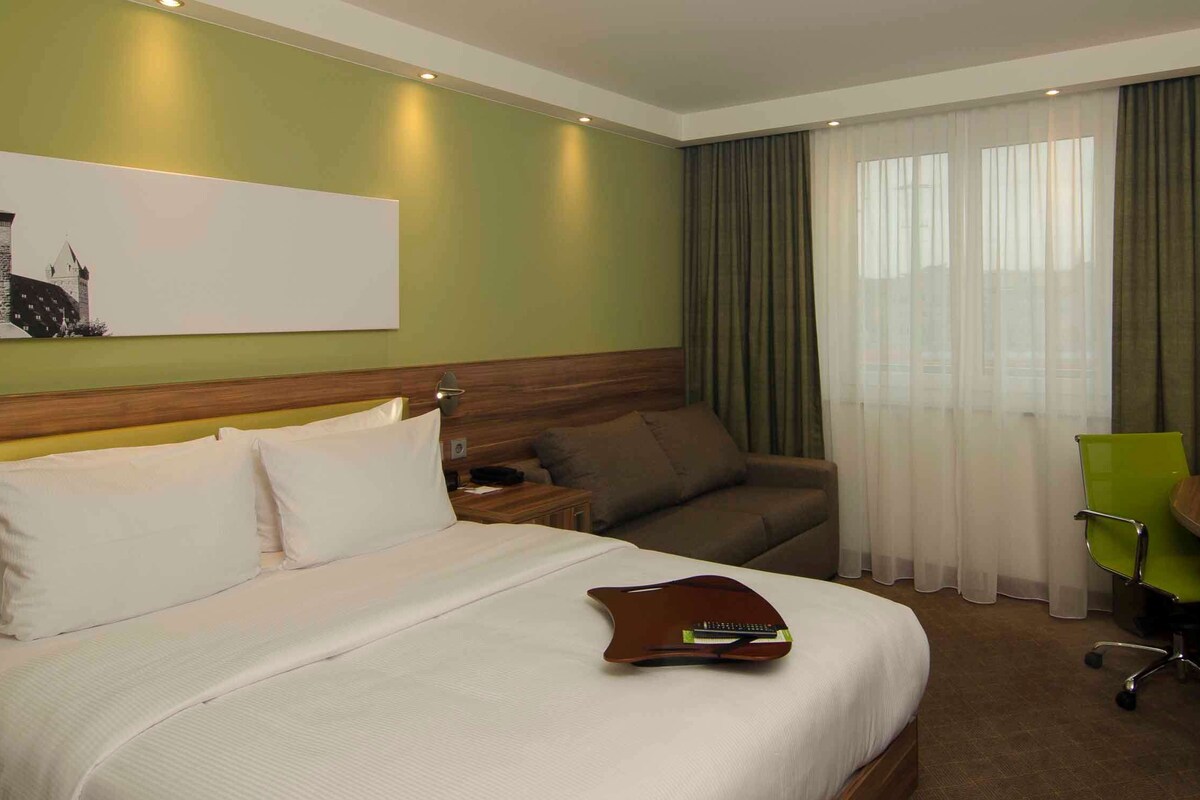 Une chambre d’hôtel avec un lit, un bureau, une chaise, une télévision et un tableau au mur.