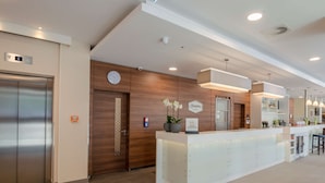 A modern reception area with a reception desk, a clock, and an elevator. - Hampton by Hilton Frankfurt City Centre (Frankfurt)